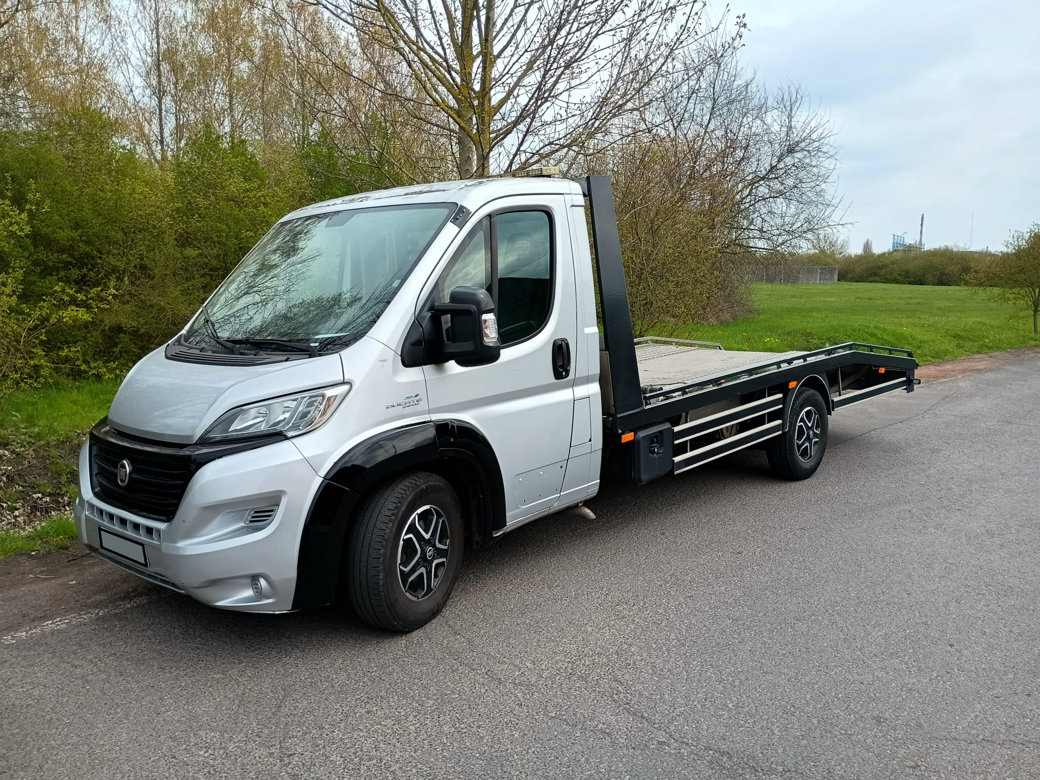Camion de remorquage jaune fluo garé en sécurité sur le bas-côté d'une route départementale dans le Nord (59), prêt à intervenir pour un dépannage ou une assistance automobile 24/7 près de Lille.