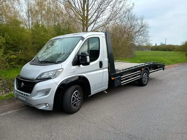 Camion de remorquage gris garé en sécurité sur le bas-côté d'une route départementale dans le Nord (59), prêt à intervenir pour un dépannage ou une assistance automobile 24/7 près de Lille.